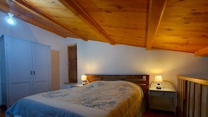 Un dormitorio con cama, dos mesitas de noche con lámparas, un armario y techo de madera.