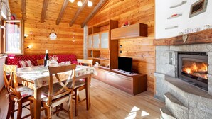 Un interior de madera con chimenea, vigas de madera en el techo, una zona de comedor y un televisor.