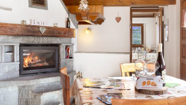 Una habitación acogedora con chimenea, vigas de madera, una mesa de comedor y una caja de Tegolet, además de una botella de vino.