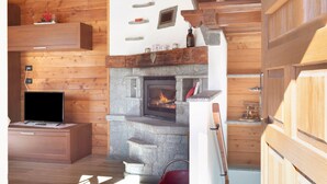 Interior acogedor de una cabaña con chimenea de piedra, paredes de madera, un televisor sobre un mueble de madera y una pequeña estantería con adornos.