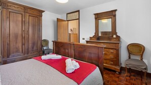 A hotel room with a bed, a wooden dresser, a chair, a mirror, and a ceiling light. - Apartment 'Maison Du Soleil - Bien-être' with Mountain View, Private Terrace and Wi-Fi (Saint-Vincent)