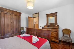 A hotel room with a bed, a wooden dresser, a chair, a mirror, and a ceiling light.