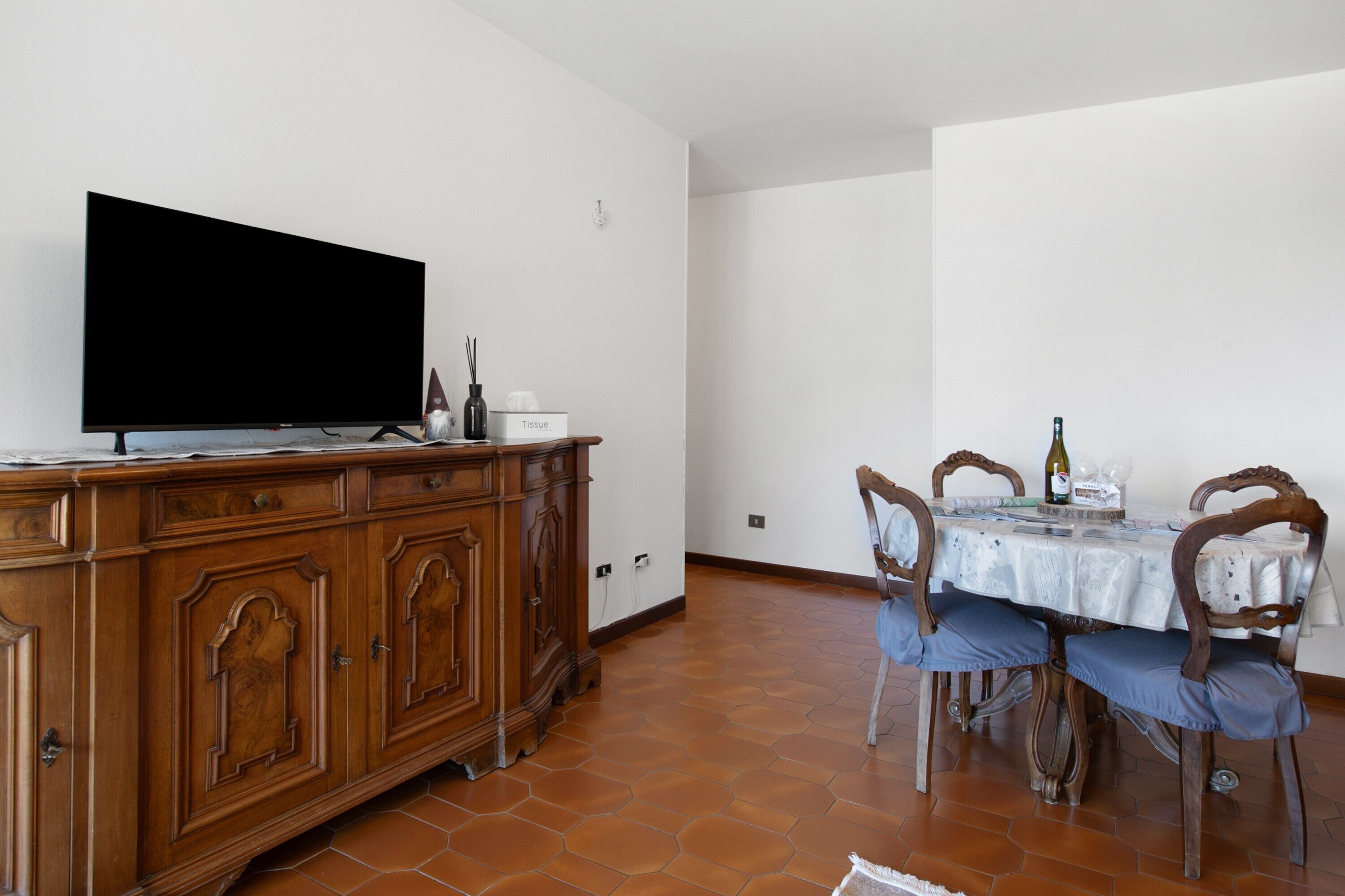 Ein Essbereich mit Tisch, Stühlen, einem Fernseher auf einem Schrank und einem Fliesenboden.