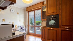 A kitchen with wooden cabinets, a built-in oven, a refrigerator, and a window with a view of greenery. - Apartment 'Maison Du Soleil - Bien-être' with Mountain View, Private Terrace and Wi-Fi (Saint-Vincent)