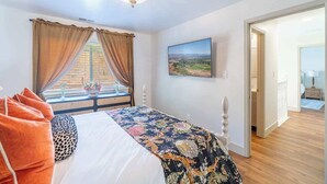 A bedroom with a bed, curtains, a chandelier, a painting, and a view through a window. - The Deco Retreat - UNR - Pet Friendly (Reno)
