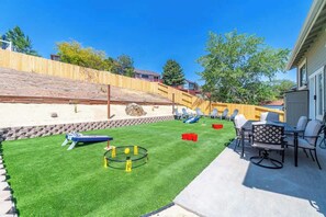 Un patio trasero con césped, un trampolín y una zona de patio con mobiliario exterior.