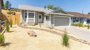 A single-story house with a garage, a front yard with rocks and plants, and a wooden fence. - The Deco Retreat - UNR - Pet Friendly (Reno)