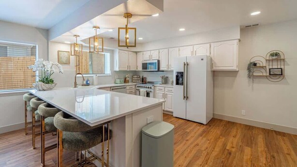 A modern kitchen with white cabinetry, a central island with bar stools, a microwave, stove, and refrigerator. - The Deco Retreat - UNR - Pet Friendly (Reno)