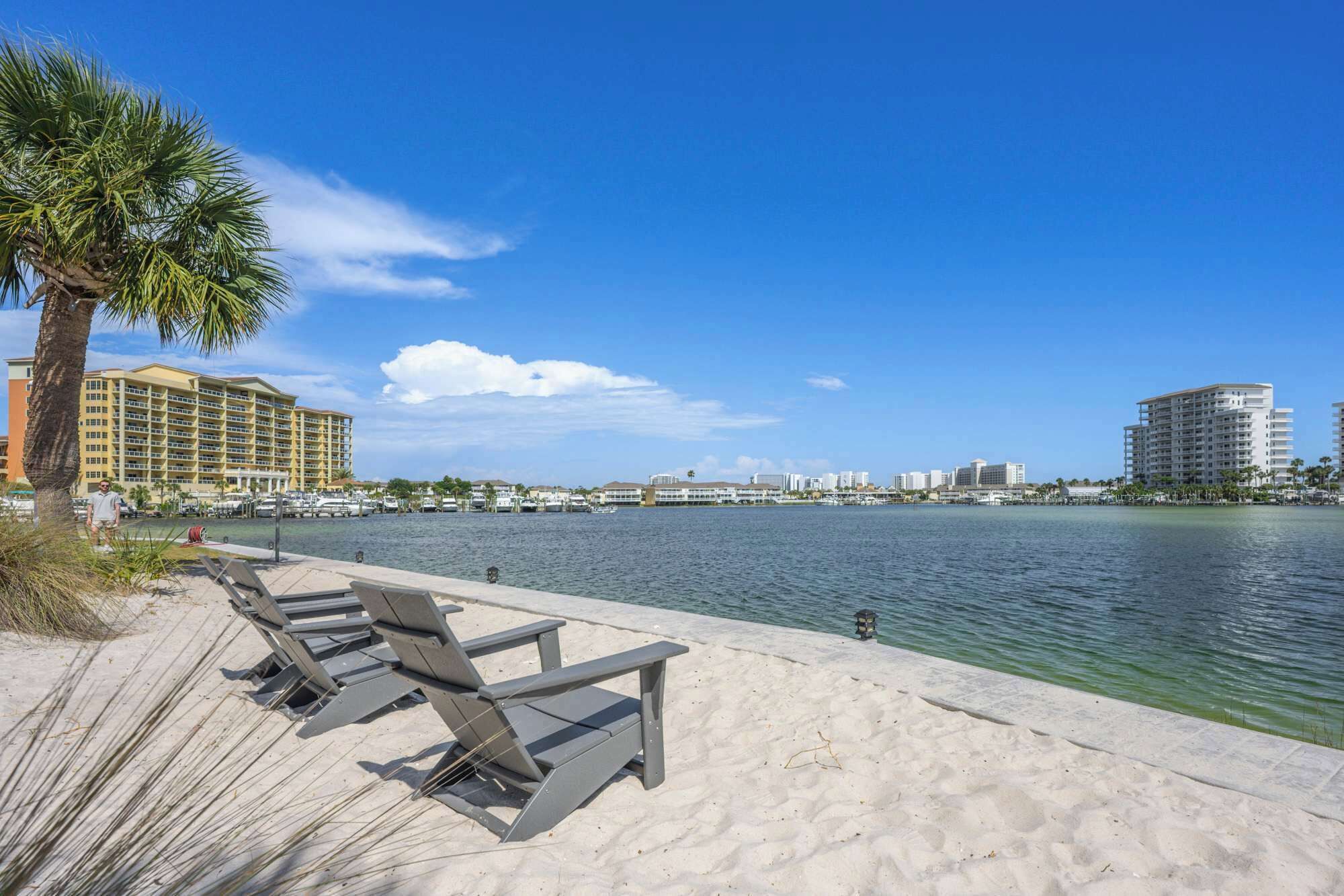 A beach with lounge chairs, a palm tree, and a marina with boats.