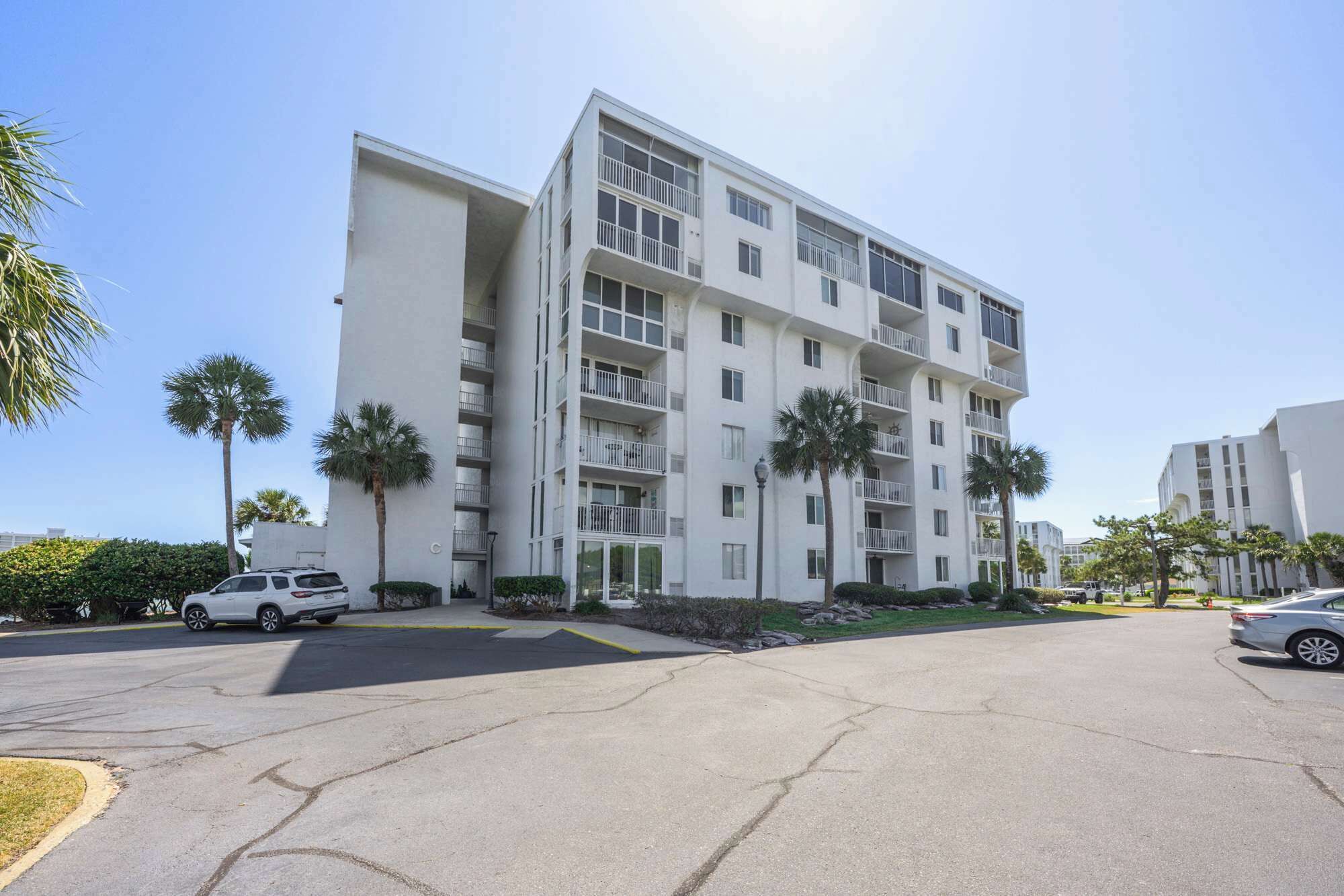 Un edificio residencial de varios pisos con balcones, estacionamiento y palmeras.