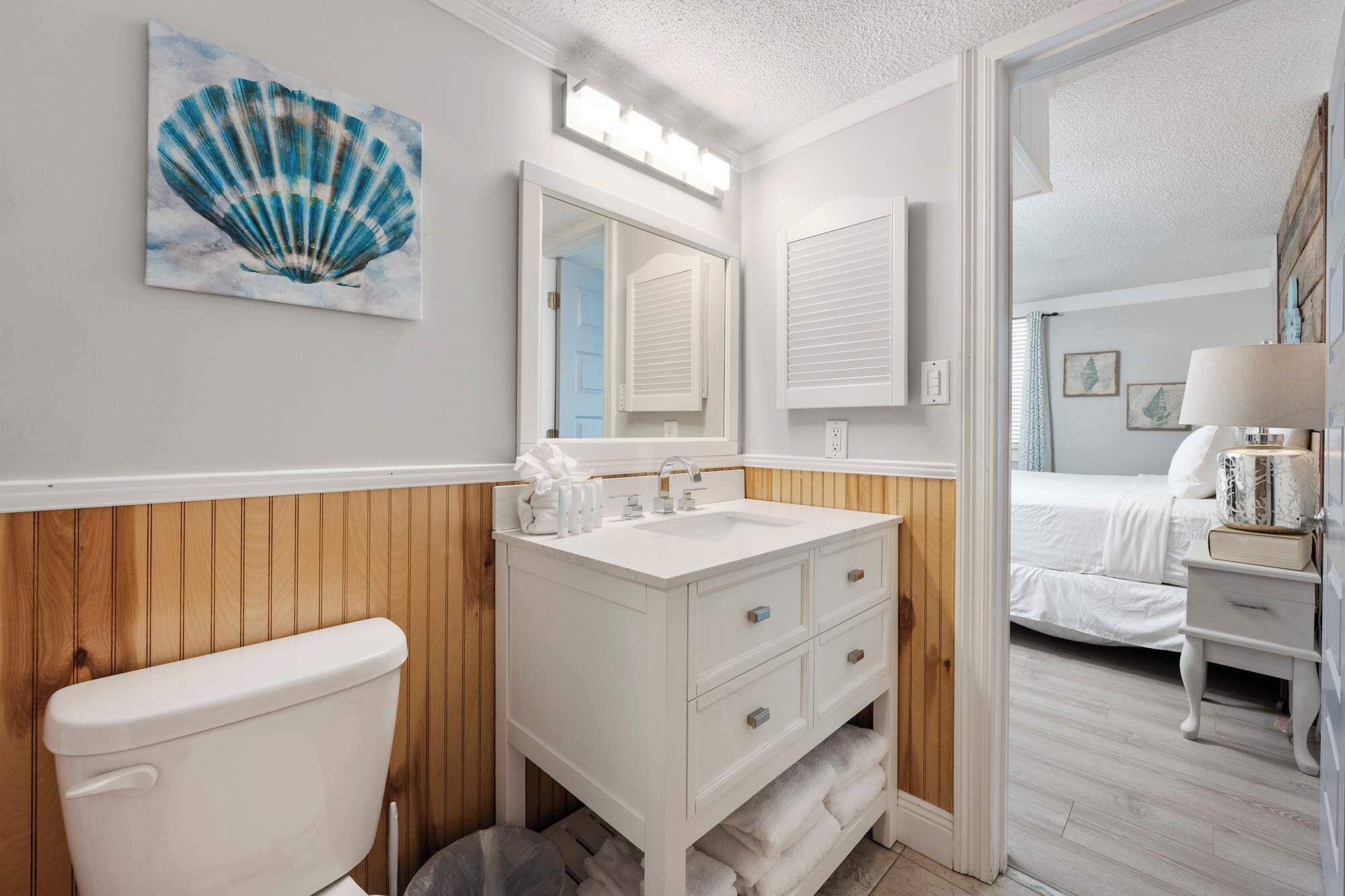 Un bagno con parete rivestita in legno, un lavandino bianco, uno specchio e un water.