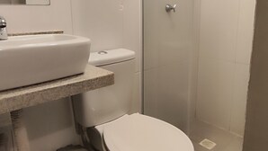 Uma casa de banho moderna com lavatório, sanita e chuveiro, tudo em branco.