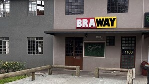 Um edifício com um letreiro 'BRAWAY', um espaço pavimentado em tijolos e um banco de madeira.