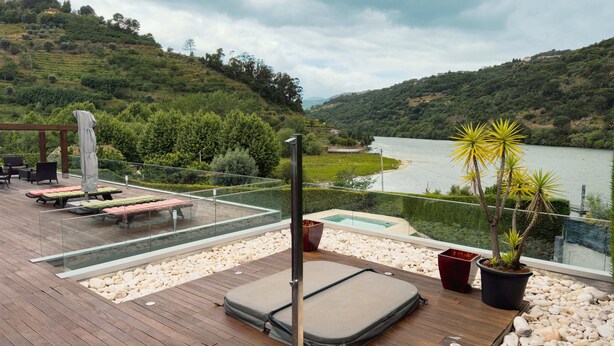 Terraza con tumbonas, una piscina pequeña y vistas a un lago rodeado de colinas.