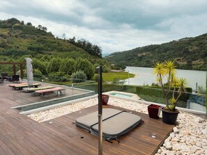 Um terraço com espreguiçadeiras, uma piscina pequena e vista para um lago rodeado por colinas.