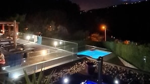 Vista nocturna de un área de piscina con jacuzzi y zona de estar cubierta.