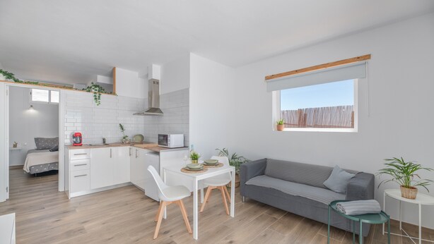 Um espaço compacto com cozinha compacta, área de refeições, sofá cinza e janela com vista.