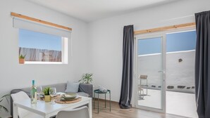 Quarto moderno com mesa de jantar, cadeiras, sofá, mesinha lateral, planta em vaso e porta de vidro deslizante para área externa.