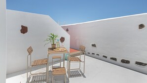 Um terraço de paredes brancas com uma mesa, cadeiras, uma planta em vaso e uma garrafa.