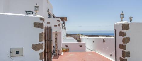 A narrow pathway leading to a white building with stone accents and a view of the sea.