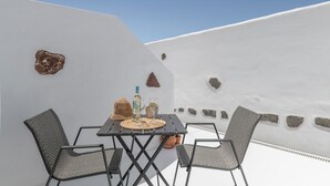 Una terrazza dalle pareti bianche con un tavolo, sedie, una bottiglia e dei bicchieri.