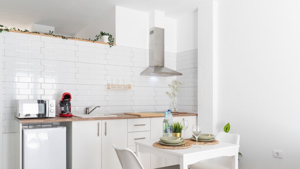 Una cucina moderna con mobili bianchi, forno a microonde integrato, macchina del caffè e un piccolo frigorifero.