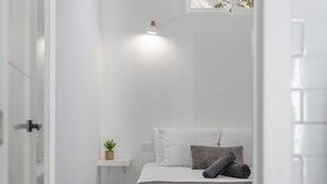 Camera da letto minimalista con un letto, un comodino, una piccola pianta e una finestra.