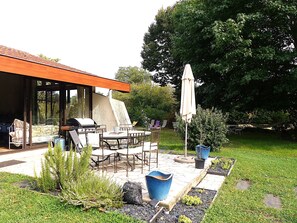 Un'area patio esterna con zona salotto coperta, barbecue e piante in vaso.