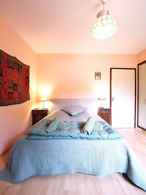 Una camera da letto con un letto grande, due comodini con lampade, un lampadario, una porta e un arazzo a parete.
