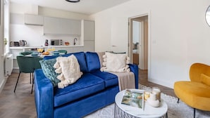 A modern living room with a blue sofa, a yellow armchair, and a dining area with a table and chairs.