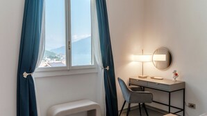 Una habitación de hotel con una cama, un escritorio con silla, un banco y una ventana con cortinas.