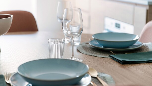 Una mesa de comedor dispuesta con platos, vasos y cubiertos.