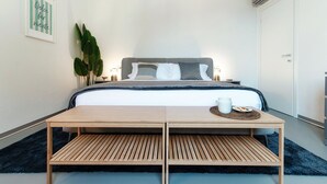 Un dormitorio moderno con cama, mesitas de noche, una planta grande y un aire acondicionado instalado en la pared.
