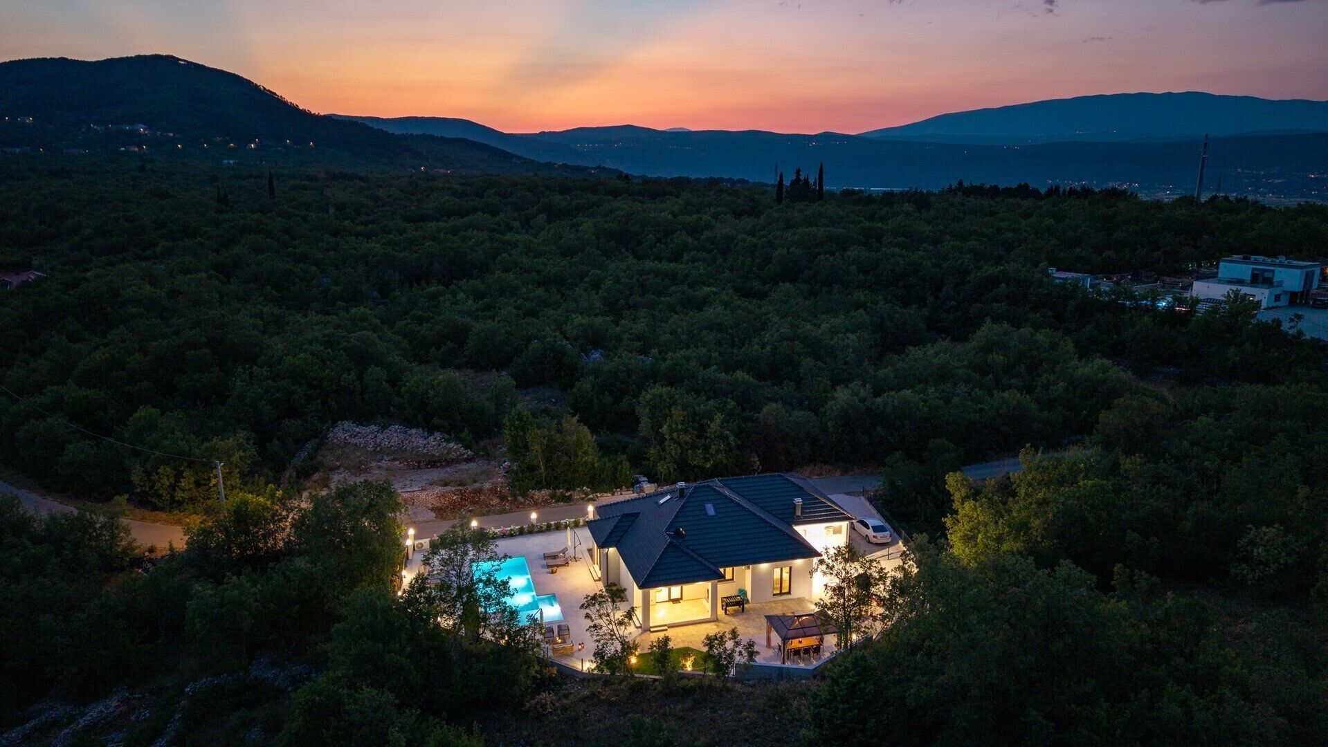 Ein modernes Haus mit Schwimmbad, umgeben von dichtem Wald und Bergen im Hintergrund.