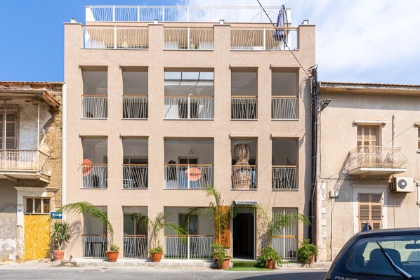 A multi-story building with balconies, potted plants, and a clear sky. - Sundrop 1-Bedroom Apartment in Larnaca (Larnaca)