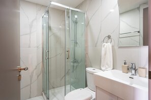 A modern bathroom with a glass-enclosed shower, a white toilet, and a vanity with a mirror and sink. - Sundrop 1-Bedroom Apartment in Larnaca (Larnaca)