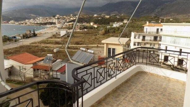 Een balkon met uitzicht op een kustplaats, zonnepanelen en een bergachtig landschap.