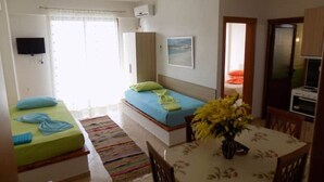 Een kamer met twee bedden, een eettafel met stoelen, een televisie en een raam met gordijnen.