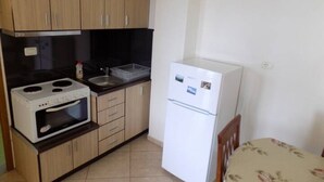 Een kleine keuken met houten kastjes, een witte kookplaat, een spoelbak en een witte koelkast.