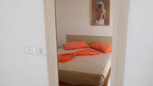 Et soveværelse med en seng, orange puder og et billede på væggen.