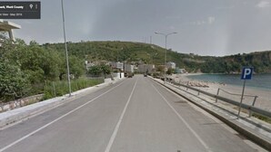A coastal road with a parking sign, a beach, and buildings in the background. - 25 meters from the beach 4 (Himarë)