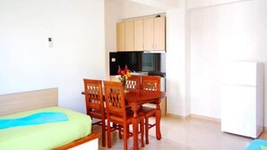 A compact living space with a bed, wooden dining table, chairs, a kitchen area with cabinets and appliances, and a small white refrigerator. - 25 meters from the beach 4 (Himarë)