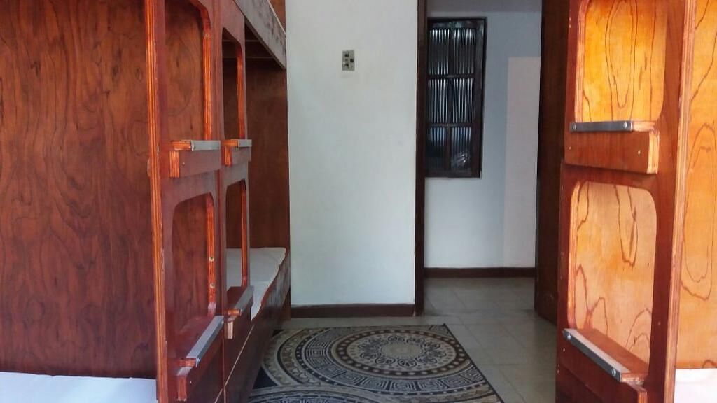 Un couloir avec des lits superposés en bois, un tapis à motifs et une fenêtre grillagée.