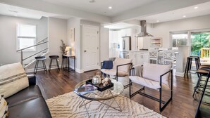 A modern living room with a sofa, armchairs, a coffee table, and a staircase leading to a kitchen. - Walk to the stadium! - Lighthouse on Glenwood (Annapolis)
