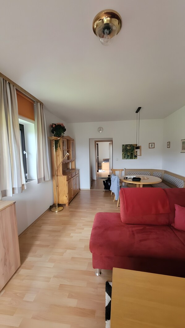 A spacious living area with a wooden floor, a red sofa, a wooden cabinet, and a dining table.