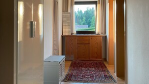 Ein Flur mit Holzboden, einem Fenster mit Blick auf Bäume, einem Holzschrank und einem blauen Teppich.