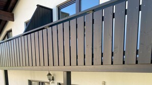 Ein zweistöckiges Gebäude mit Balkon, einem fenster mit Vorhang und einer Tür mit einem Metallgitter.