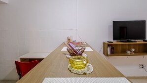 Un salón moderno con una mesa de comedor de madera, una silla roja, un televisor sobre un mueble de madera y una pared blanca.