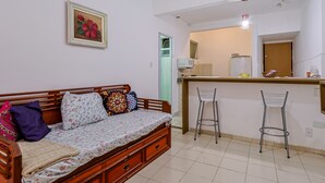 Una habitación con un sofá de madera, una pequeña zona de cocina con un taburete y una puerta que da a otra habitación.