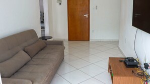 Un salon avec un canapé marron, une porte en bois, une petite table et un téléviseur fixé au mur.